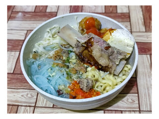 Bakso. A bowl of rib meatballs with yellow noodles, blue vermicelli, shredded cabbage, fried onions and chili sauce on a wooden patterned table. The meatballs look very delicious and delicious.