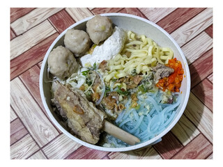 Bakso. A bowl of rib meatballs with yellow noodles, blue vermicelli, shredded cabbage, fried onions and chili sauce on a wooden patterned table. The meatballs look very delicious and delicious.