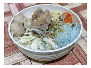 Bakso. A bowl of rib meatballs with yellow noodles, blue vermicelli, shredded cabbage, fried onions and chili sauce on a wooden patterned table. The meatballs look very delicious and delicious.