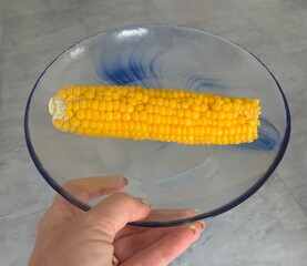 Woman holding a corn on the cob on a glass plate
