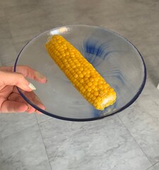 Woman holding a corn on the cob on a glass plate