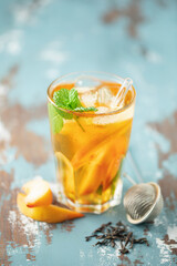 Fruit black iced tea with peaches and mint in a glass on the table. Summer drink concept