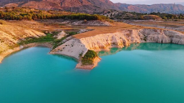 Drone video showing turquoise waters and rocky shoreline in Spain, with golden hour sunlight highlighting the rugged cliffs and surrounding landscape.