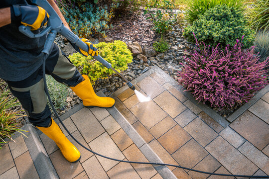 Person Cleaning Paver Stones in Garden With Pressure Washer on Sunny Day