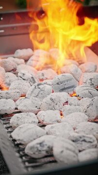 Close-up of white-hot charcoal briquettes with bright orange flames rising on a barbecue grill, ready for outdoor cooking.
