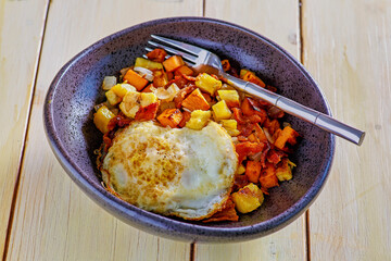 sweet potato and plantain hash topped with a fried egg, fork in bowl