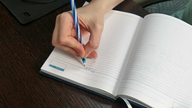 Close-up of open daily planner on brown wooden desk. Woman writes the word PLAN and numbers tasks from 1 to 10, organizing her schedule for effective time management. - Powered by Adobe