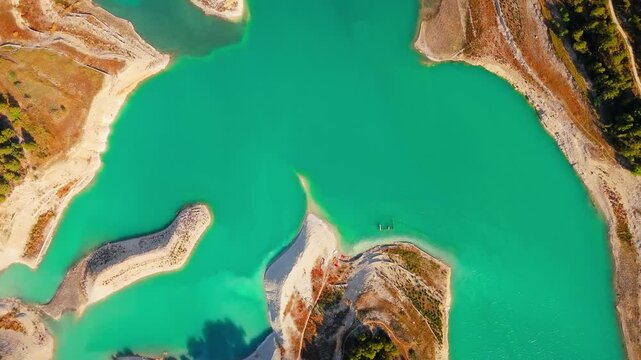 Drone video of the turquoise Guadalest Reservoir in Spain, surrounded by green hills and mountains, showing vivid water colors and scenic Mediterranean landscapes.