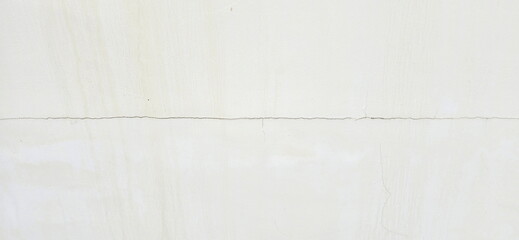 The white wall has cracks. External cracks in building. Cracks on wall are straight lines from left to right. Building problems and solutions. Damage from subsidence, vibration.Cracked wall background
