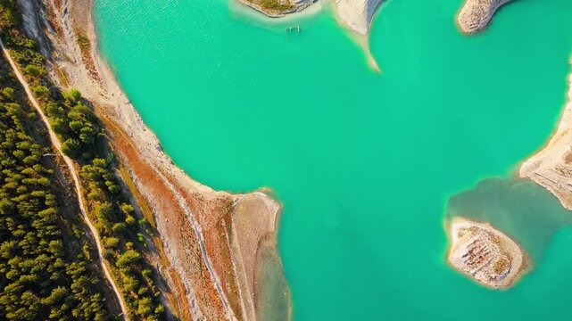 Drone video of the turquoise Guadalest Reservoir in Spain, surrounded by green hills and mountains, showing vivid water colors and scenic Mediterranean landscapes.
