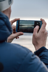person wearing winter coat and hat takes photo stunning sunrise over peaceful frozen lake. ice reflects colors sky, creating tranquil atmosphere. vertical. close up.