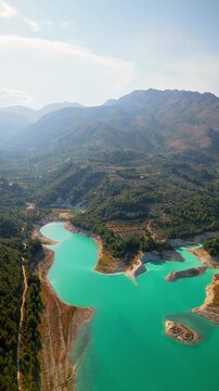 Drone video of the turquoise Guadalest Reservoir in Spain, surrounded by green hills and mountains, showing vivid water colors and scenic Mediterranean landscapes.