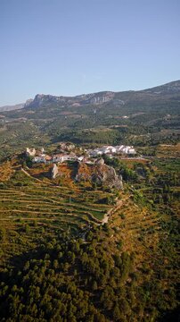 Drone video of the historic hilltop village of Guadalest in Spain, showcasing its ancient castle, charming houses, and surrounding mountains under clear blue skies.