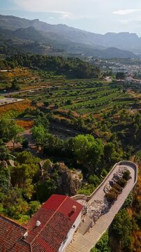 Drone video of the historic hilltop village of Guadalest in Spain, showcasing its ancient castle, charming houses, and surrounding mountains under clear blue skies.