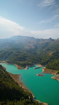 Drone video of the turquoise Guadalest Reservoir in Spain, surrounded by green hills and mountains, showing vivid water colors and scenic Mediterranean landscapes.
