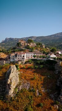 Drone video of the historic hilltop village of Guadalest in Spain, showcasing its ancient castle, charming houses, and surrounding mountains under clear blue skies.