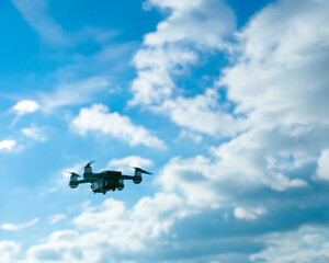 Black drone flying against bright blue sky with white fluffy clouds