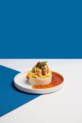 A serving of rice topped with soft scrambled eggs, crispy karaage chicken, special savory sauce, and fresh chili and scallion garnish on a minimalist white plate with a modern white & blue background.