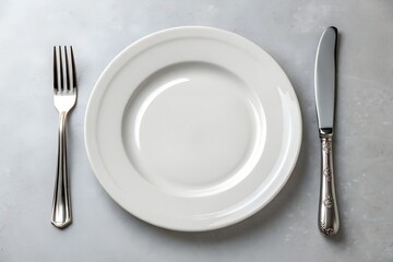 An empty white plate with a fork and knife set on a grey surface, symbolizing a clean slate for dining, meal preparation, or a minimalist culinary presentation