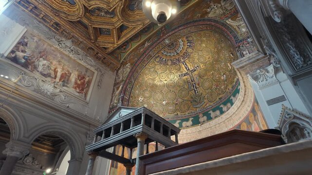 Close view of basilica apse with golden mosaic, crucifix and row of saint frescoes under detailed coffered ceiling
