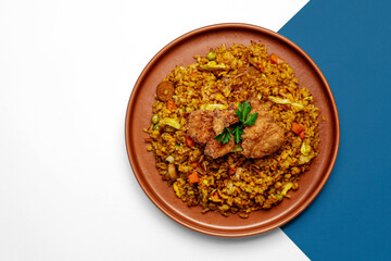 A plate of Indonesian fried rice (nasi goreng) with fried chicken on top, garnished with fresh parsley. Traditional Asian cuisine with vegetables and spices. Top view minimal white and blue background