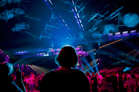 Silhouetted audience watching stage performance with dramatic blue and purple concert lighting
