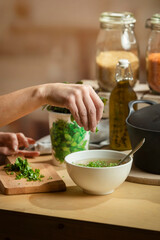 Hand garnishing soup with fresh herbs while cooking ingredients and oil bottle are arranged nearby