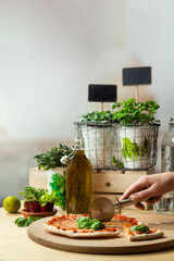 Hand cutting pizza with lime, fresh herbs, and cooking ingredients arranged on wooden surface