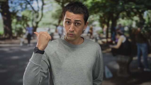 Man hand showing thumbs down gesture in street under trees during daylight outdoors; dismissal disapproval.