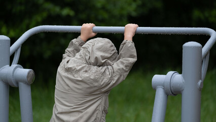 Child hanging on outdoor exercise bar in hooded jacket
