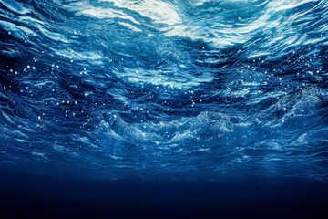 Sunlight filters through the ocean surface, creating a glimmering effect on the waves above, contrasting with the deep blue water below