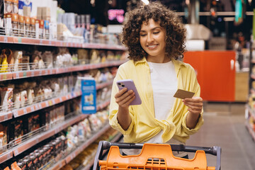 Woman Using Smartphone and Credit Card While Shopping in Supermarket