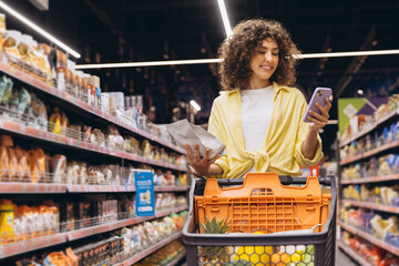 Woman using smartphone and choosing food in supermarket