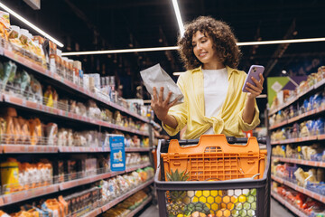 Woman using smartphone and choosing groceries in supermarket