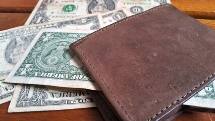 Leather wallet with a dollar bill inside on top of other dollar bills on a wooden background