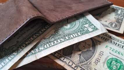 Open leather wallet on top of dollar bills on a wooden background