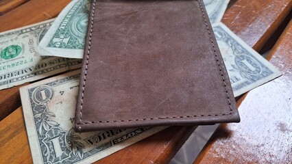 Open leather wallet on top of dollar bills on a wooden background
