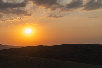 Two silhouettes of people on a hill against the backdrop of a colorful sunset.