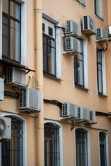 Facade of building with many air conditioners on windows in southern hot country. Yellow house exterior on city street. Escape from heat, creating favorable microclimate in urban apartments concept.