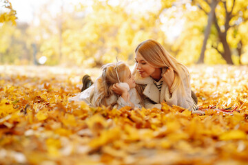 Happy mother and daughter having fun in an autumn park at sunset. Young woman with her beloved daughter throwing autumn leaves up and spending time together outdoors. Fun and childhood concept.