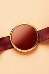 A shiny maroon oval with a gold border, wrapped with a diagonal maroon textured ribbon on a light beige background. Concept of award, gift, elegant, simple.
