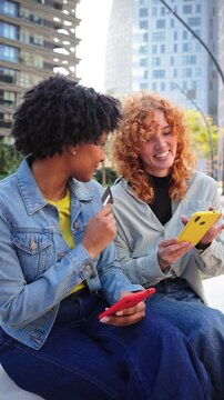 Two cheerful women are engaged in an online shopping experience, using their smartphones while handling a credit card for a seamless purchase. They share a moment of joy while shopping together.