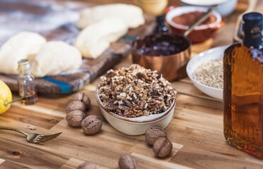 On a wooden table, baklava ingredients await transformation into a golden, nutty delicacy. Dough rests near chopped walnuts, a golden syrup bottle, and a bright lemon, all bathed in soft light