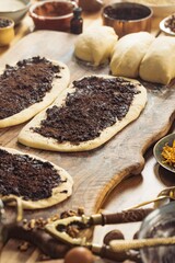In a warm lit kitchen, dough sits ready. Poppy seed filling is generously added to stretched dough, preparing for baking. Nuts and old tools surround the process