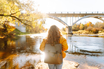 A rear view of a young female hiker with a backpack on a hiking trail in autumn enjoying sunlight....