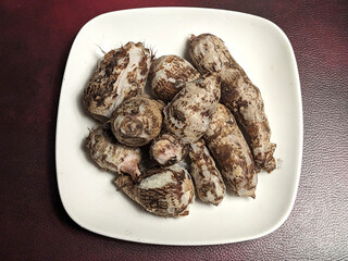 A plate of raw taro roots with their textured brown and white skin and fibrous texture displayed on a white square plate.