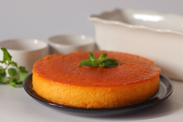 Caramel bread pudding with a glossy amber top, garnished with fresh mint leaves and served on a black plate