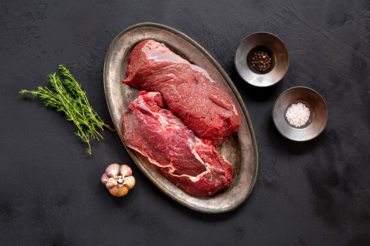 Raw beef chop on a plate. Animal product, red meat on black background top view - Powered by Adobe