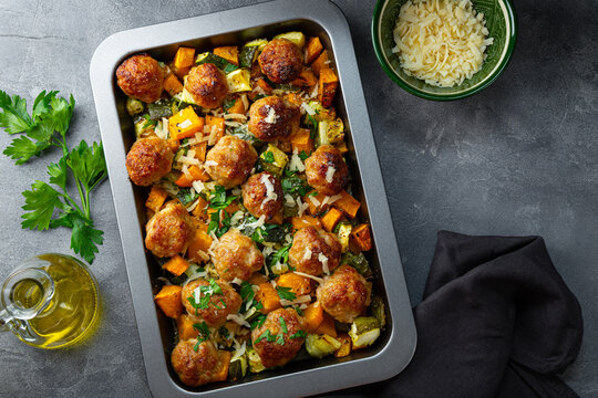 Meatballs on a vegetable bed of pumpkin and zucchini on a baking sheet and gray background, copy space for text