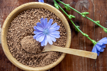 Ground chicory root in a wooden cup and chicory flowers on a rustic wooden background. Alternative medicine. Healthy drinks. chicory drink